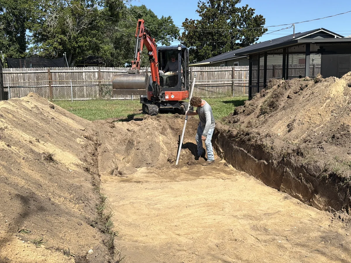 A mini excavator opening a trench in a back yard for drain field work