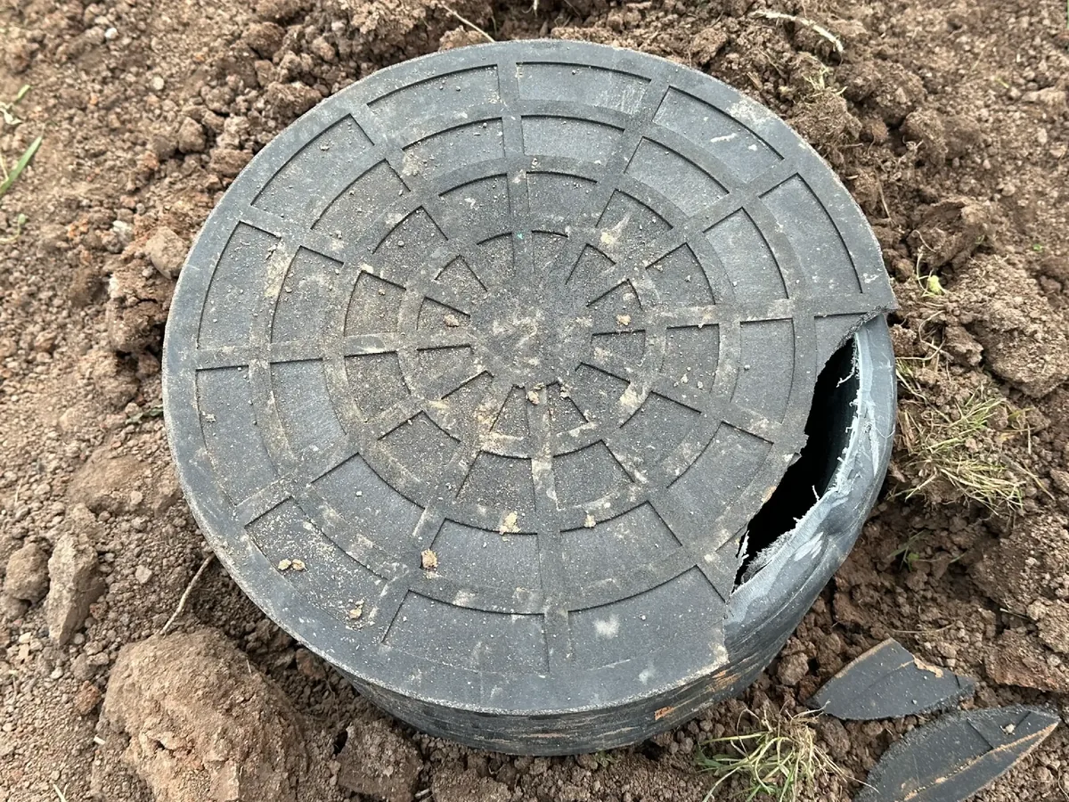 A cracked septic tank lid uncovered in the ground with broken pieces beside it