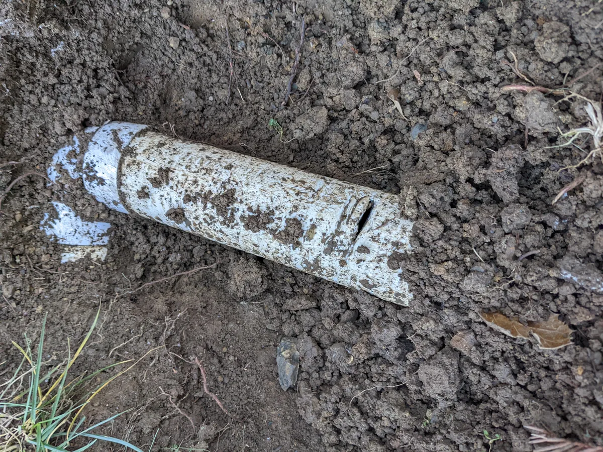 A cracked septic line uncovered in an open trench before the damaged section is replaced