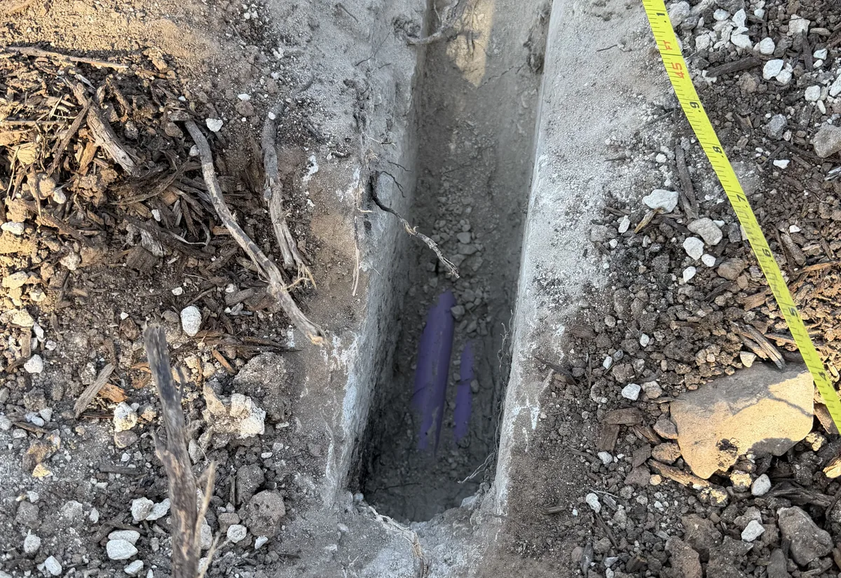 An open trench with a septic line at the bottom and a tape measure across the excavation