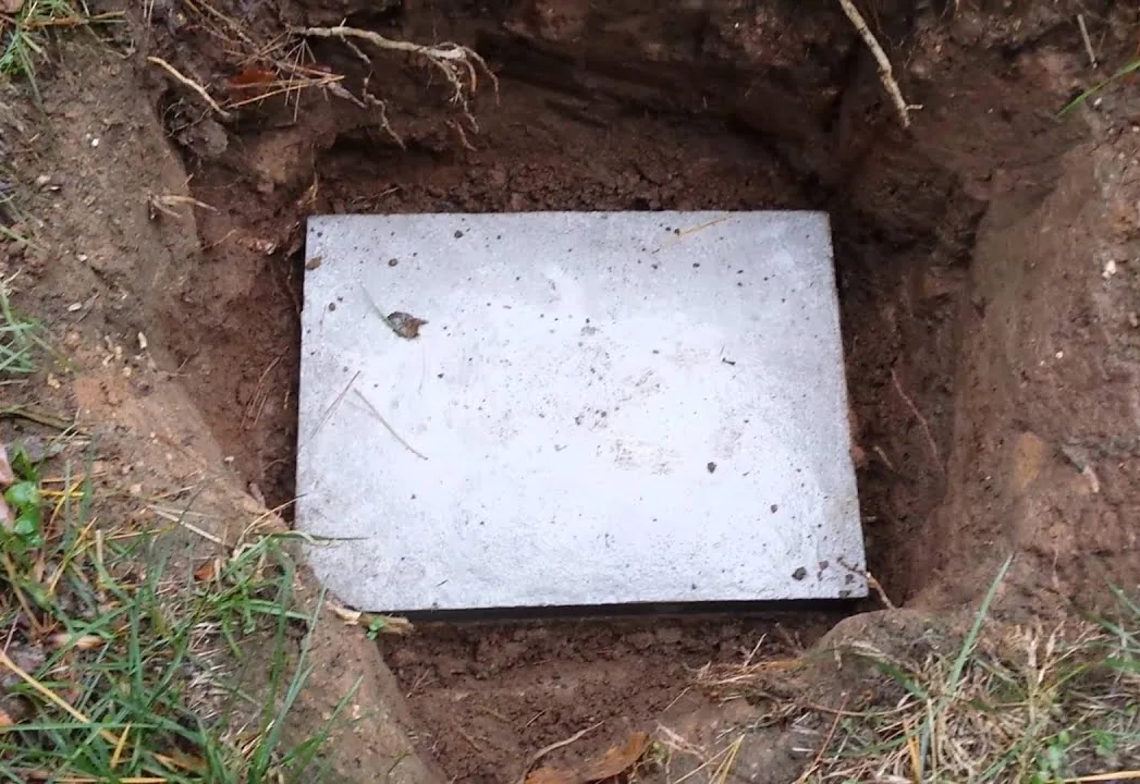 A concrete septic tank lid uncovered in a freshly dug hole