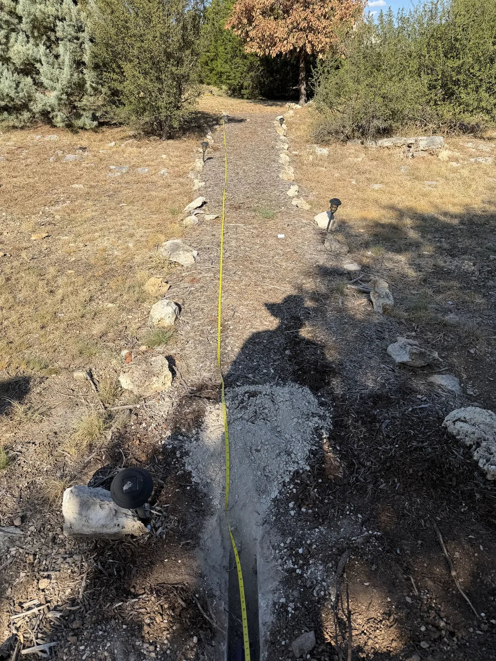 A tape measure run along a narrow trench cut across a landscaped path