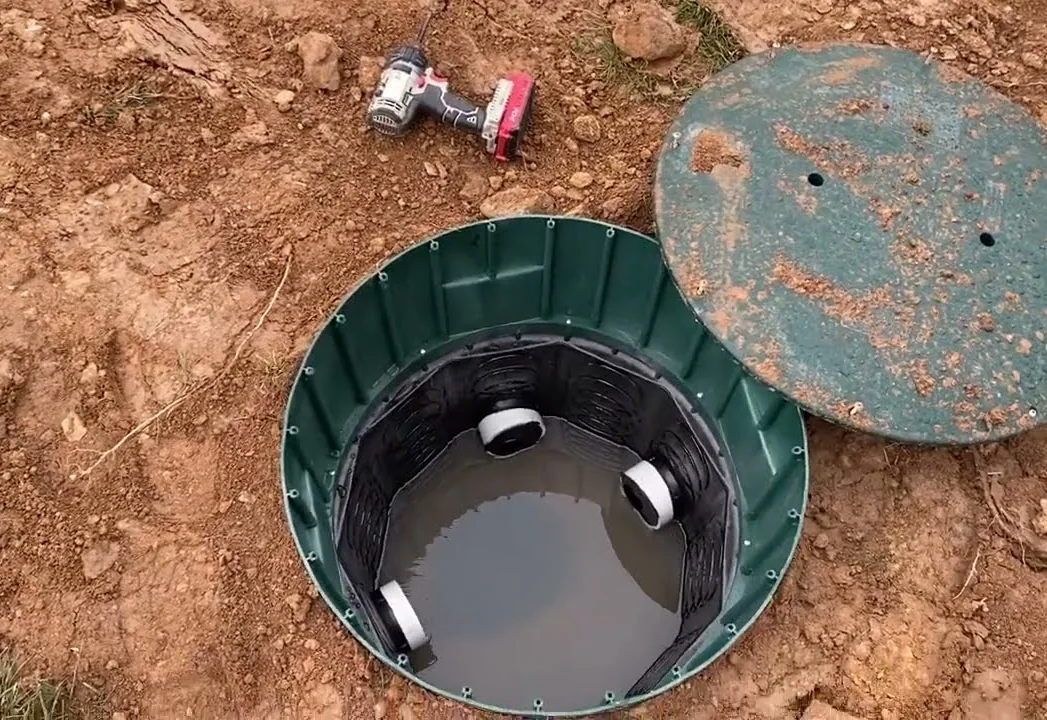 A septic riser uncovered with its lid set beside it on the ground