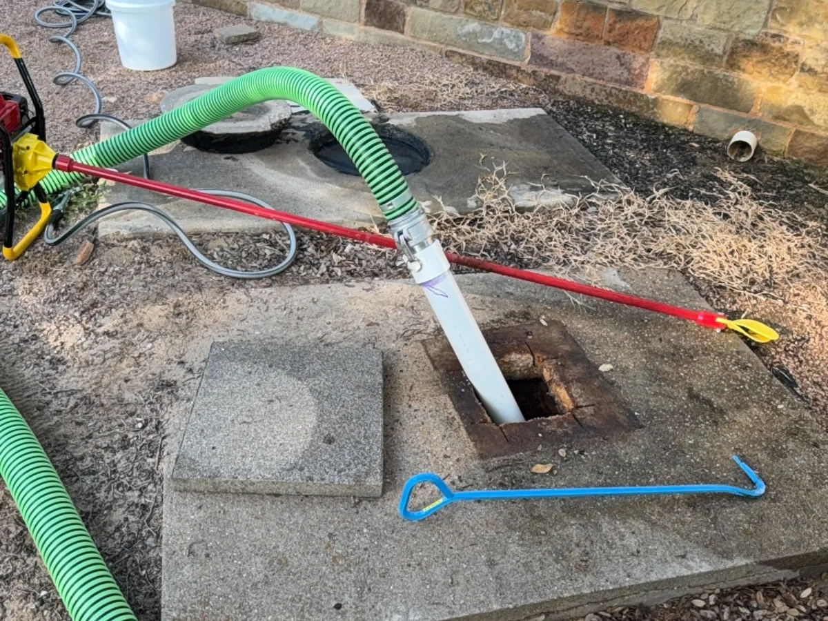 Septic tank pumping in progress with the suction hose in an open tank lid and hand tools laid out beside it