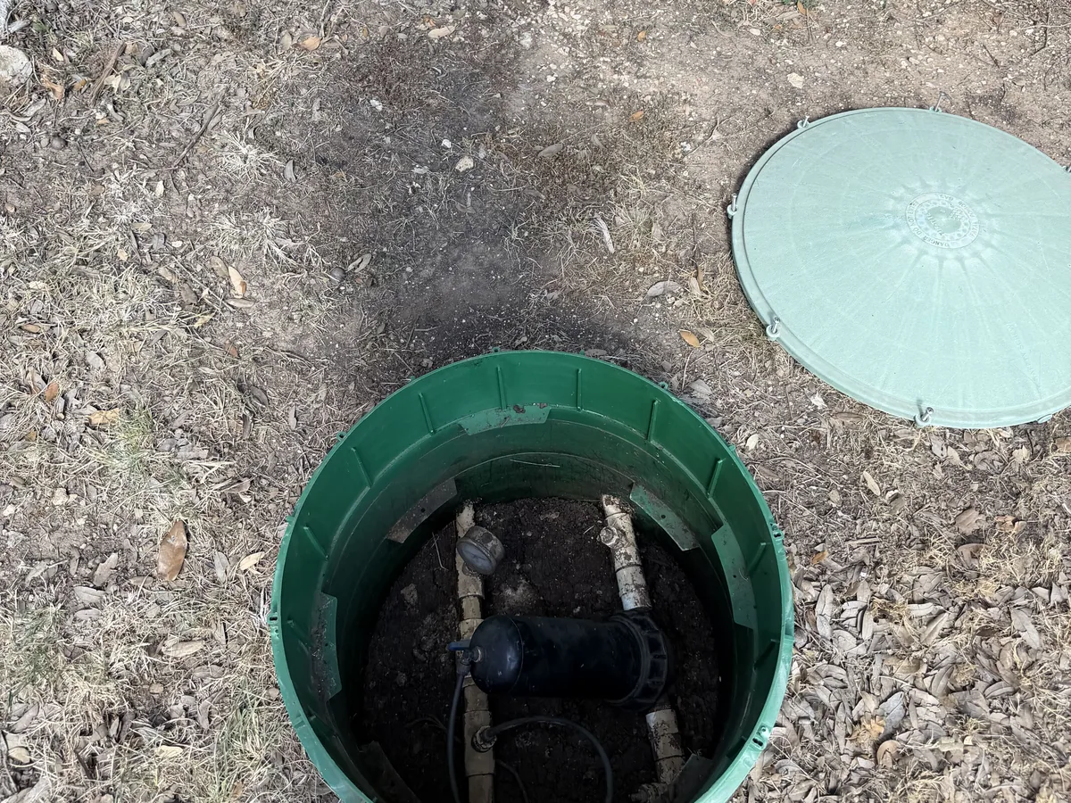 A green septic riser opened at grade with its lid set beside it
